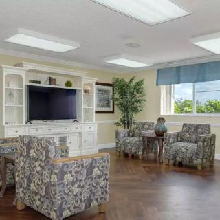 A cozy living room with patterned armchairs, a large TV, and natural lighting.