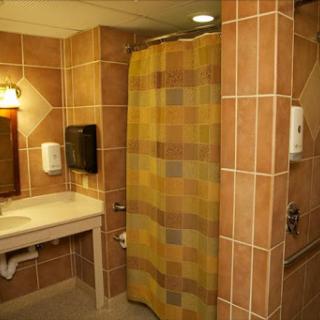 A view of a well-maintained public bathroom featuring a shower stall, sink, and tiled walls.