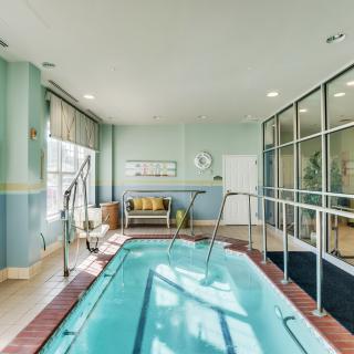 A brightly lit indoor therapy pool with handrails and large windows.