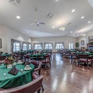 A spacious dining room with green tablecloths and elegant lighting.