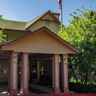 A house with a covered porch and columns, surrounded by trees, featuring a flagpole.