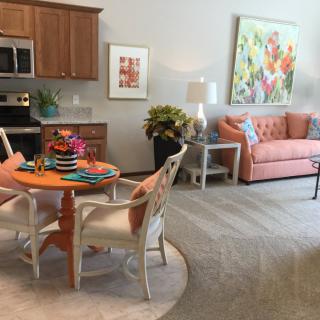 A cozy living and dining space with an orange sofa, vibrant artwork, and a compact kitchen area.