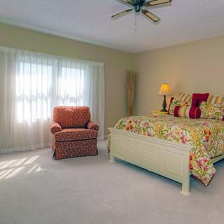 A cozy bedroom with a bed, a comfortable chair, and large windows letting in natural light.
