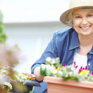 A woman smiling while gardening outside with flowers.