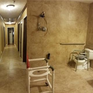 Accessible bathroom with grab bars and a shower chair next to a hallway.