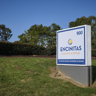 A sign at the entrance of the Encinitas building against a backdrop of trees and clear blue sky.
