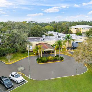 Aerial view of a hotel surrounded by greenery and parked cars.