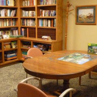 A cozy library room with wooden bookshelves and a meeting table surrounded by chairs.