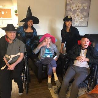 A group of people dressed in Halloween costumes, wearing various hats, posing for a photo indoors.