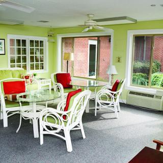 A bright sunroom with wicker furniture, glass tables, and large windows.