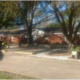 A suburban brick house with a driveway and trees in the front yard.