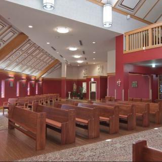 Interior view of a church featuring wooden pews and red walls.