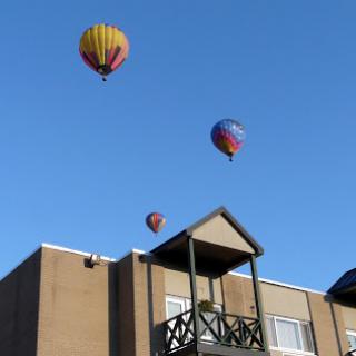 Colorful hot air balloons floating above a building under a clear blue sky.