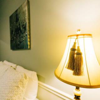 A cozy bedroom corner with a warmly lit lamp and soft bedding.