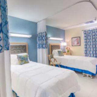 A brightly lit hospital room with two neatly made beds and blue-accented decor.