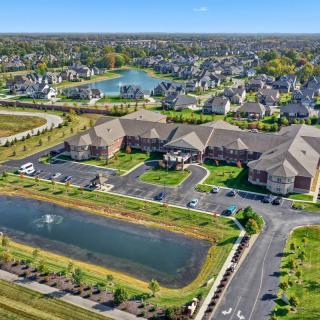 Aerial view of a suburban neighborhood featuring buildings, roads, and a pond surrounded by greenery.