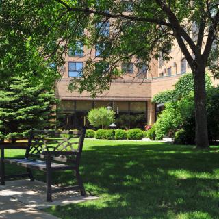 A peaceful garden area with benches and lush greenery in front of a building.
