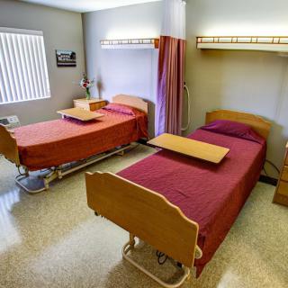 A hospital room with two beds, side tables, and a privacy curtain.