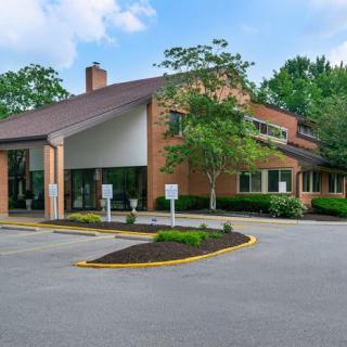 A two-story brick office building surrounded by trees with a well-maintained parking lot.