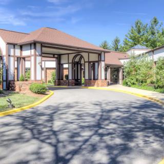 A sunny day view of a building entrance with a driveway and greenery.