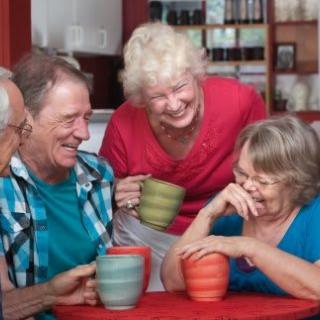 A group of seniors enjoying coffee and laughter together indoors.