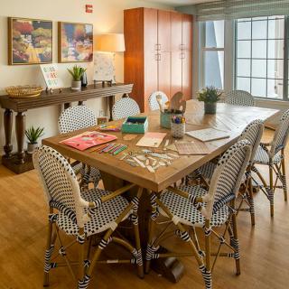 A cozy dining area with a wooden table, surrounded by patterned chairs, artwork on the walls, and lush plants adding a touch of nature.