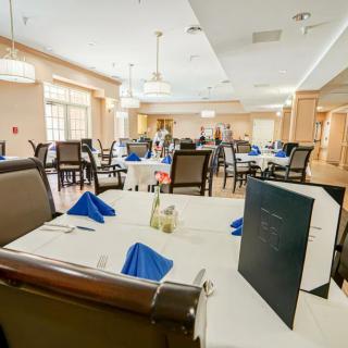 An elegant dining room with tables set for a meal, featuring blue napkins and menus on each table.