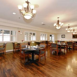 A spacious dining room with wooden floors, furnished with multiple tables and chairs, elegantly lit by chandeliers.