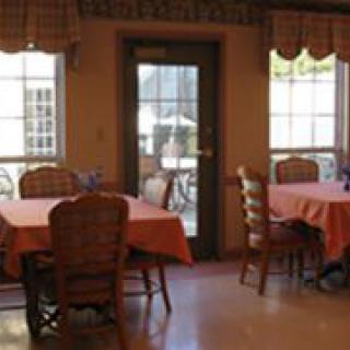 A cozy dining room with tables and chairs, featuring large windows and a door leading outside.