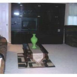 A living room featuring a coffee table with a green vase, an entertainment center with a television, and carpeted flooring.