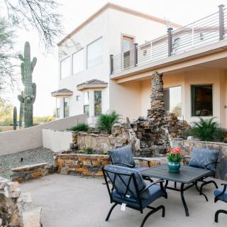 A serene outdoor patio with a stone fountain set in a desert landscape, featuring comfortable patio furniture and distinctive cacti surroundings.