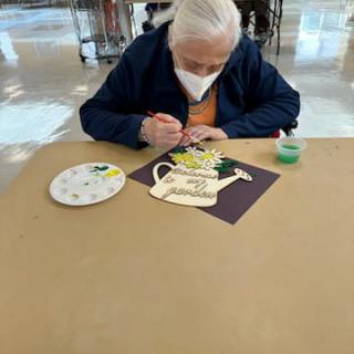 An elderly person engaged in a painting activity while wearing a mask, surrounded by art supplies.