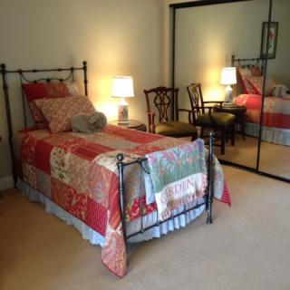 A cozy bedroom with a single bed adorned with a patchwork quilt, reflecting in a mirrored closet door.