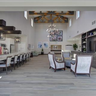 A spacious and modern living room with high ceilings, featuring a chandelier, comfortable seating, and a kitchen bar area.