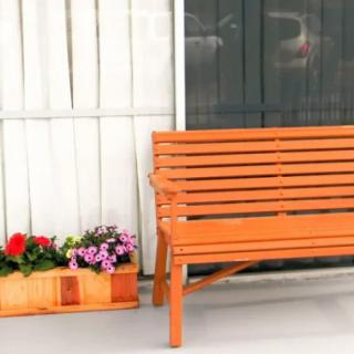 An orange bench next to a planter box with colorful flowers.