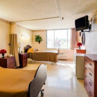 A clean and organized hospital room with two beds, a TV, and a window providing natural light.