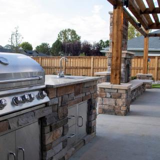 A stylish outdoor kitchen with a barbecue grill and stone countertops under a wooden pergola.