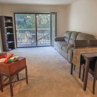 A cozy living room with a sofa, bookshelf, and sliding glass doors leading to a balcony.