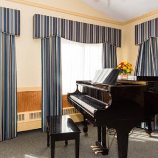 A beautifully arranged music room featuring a grand black piano and elegant striped curtains.