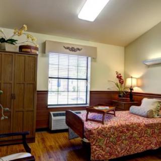 A cozy bedroom with a single bed and wooden furniture, featuring a large window and soft lighting.
