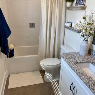 A neatly arranged bathroom with a granite countertop, white cabinets, and a shower area with a curtain.
