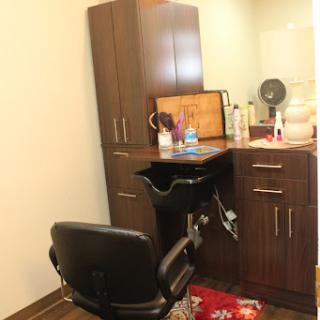 A view of a hair salon setup featuring a styling chair, wooden cabinetry, and various cosmetic products.