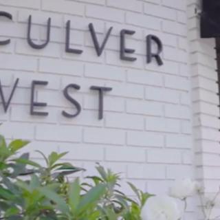 A close-up view of a building sign for Culver West with some greenery in the foreground.