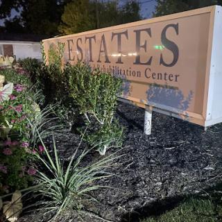 A well-lit sign for an estates rehabilitation center surrounded by plants, captured at night.