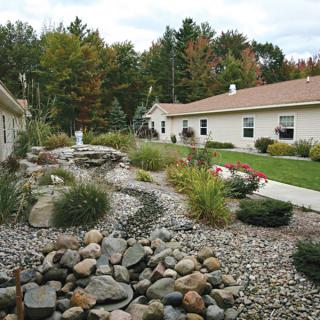 A beautifully landscaped yard featuring a rock garden and lush greenery in front of a house.