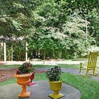 A peaceful outdoor patio with colorful planters and a yellow rocking chair overlooking a lush garden.