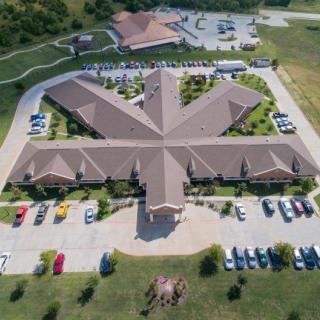 Aerial view of a uniquely designed building surrounded by a parking lot and landscaped greenery.