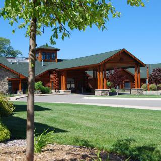 A modern building with a wooden facade set against a clear blue sky, surrounded by well-maintained grass and trees.