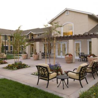 A serene courtyard with patio chairs and a pergola, surrounded by landscaped greenery.