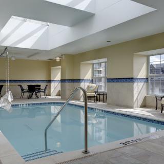 A serene indoor pool area with ample natural light from skylights and windows, surrounded by seating and tables.
